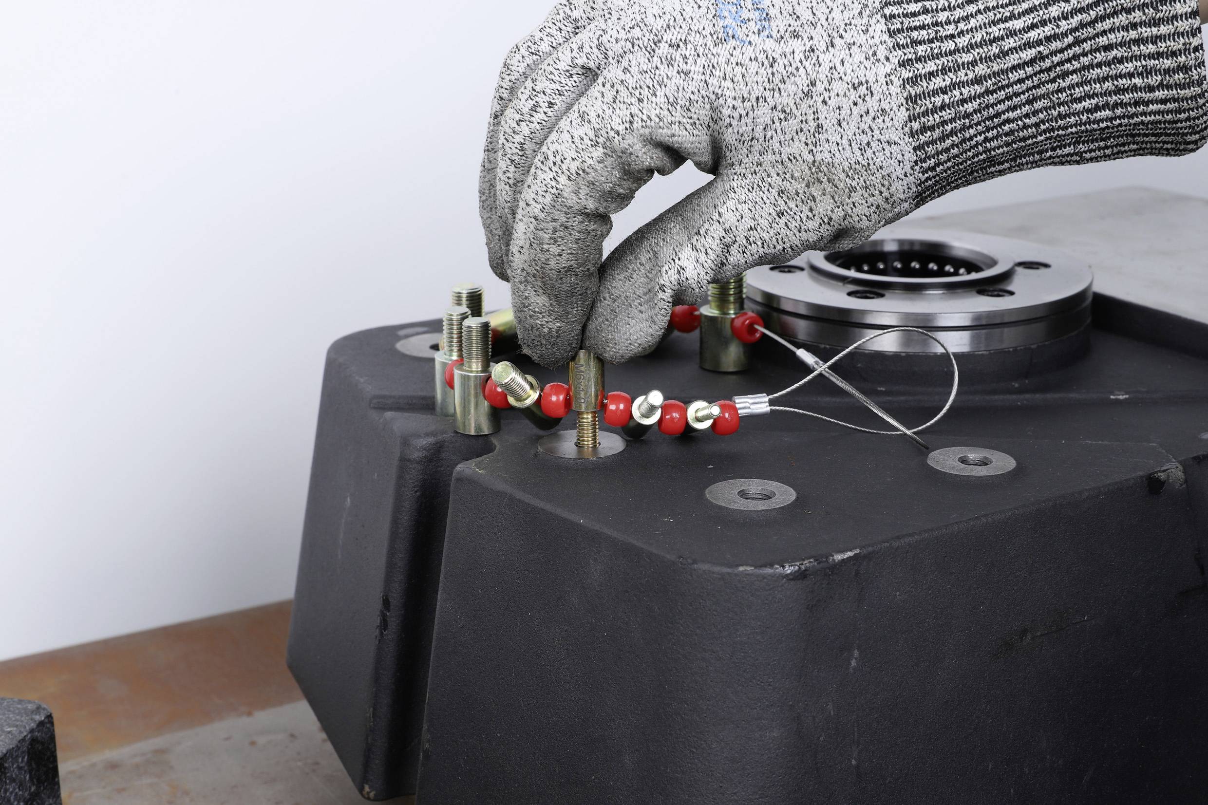 Hand met beschermende handschoen past rode parelketting aan op een metalen onderdeel in de werkplaats.