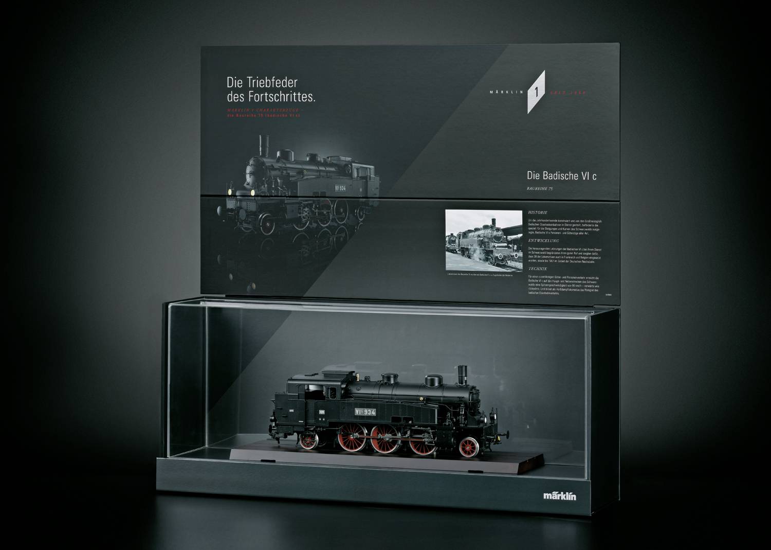 Zwart model van een stoomlocomotief in een glazen kast. Achtergrondtekst: 'De drijvende kracht van vooruitgang'. Modelnummer: 'Badische VI c'.