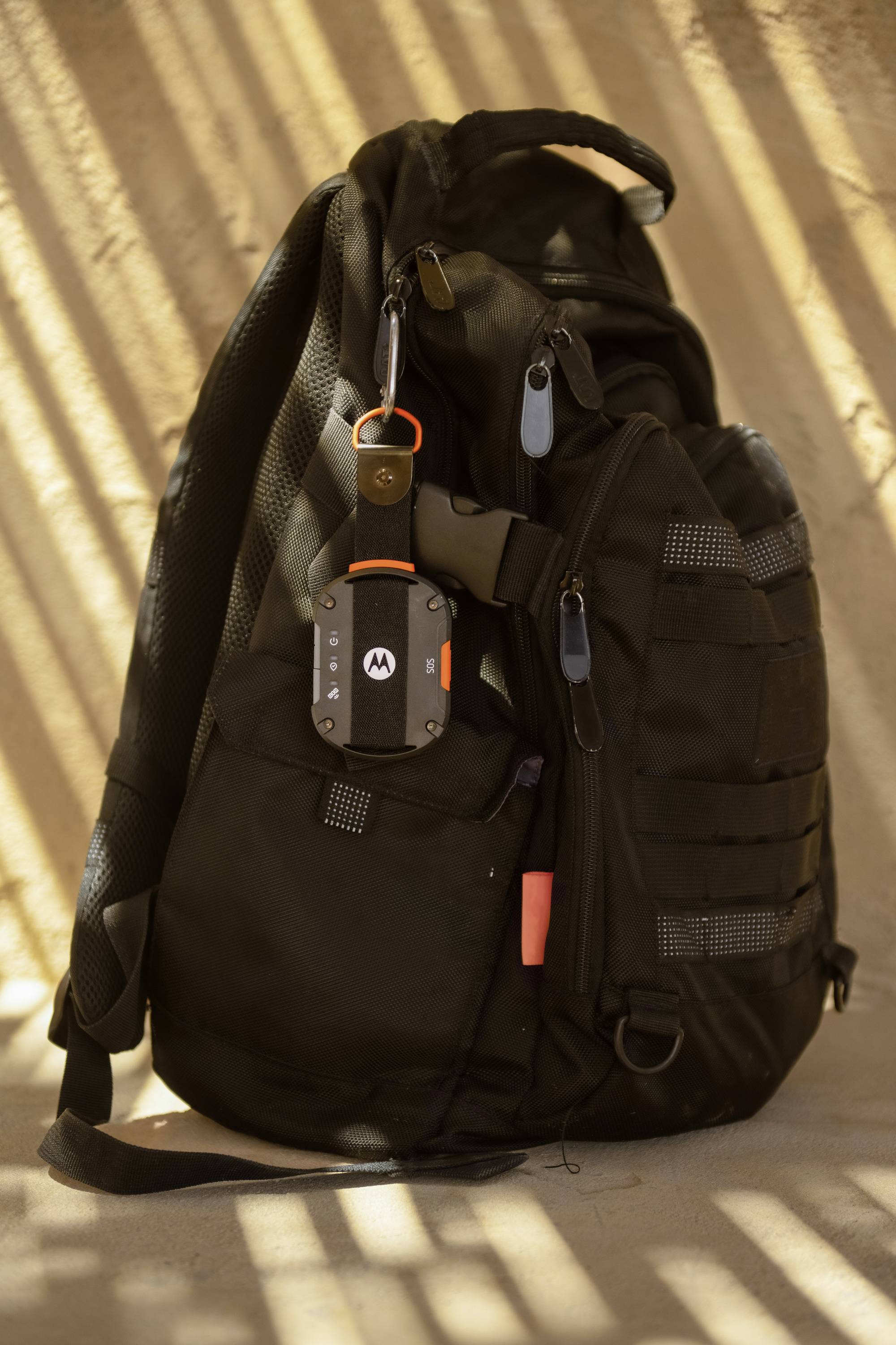 Een zwarte rugzak staat in het zonlicht. Eraan hangt een metalen voorwerp met een Motorola-logo.