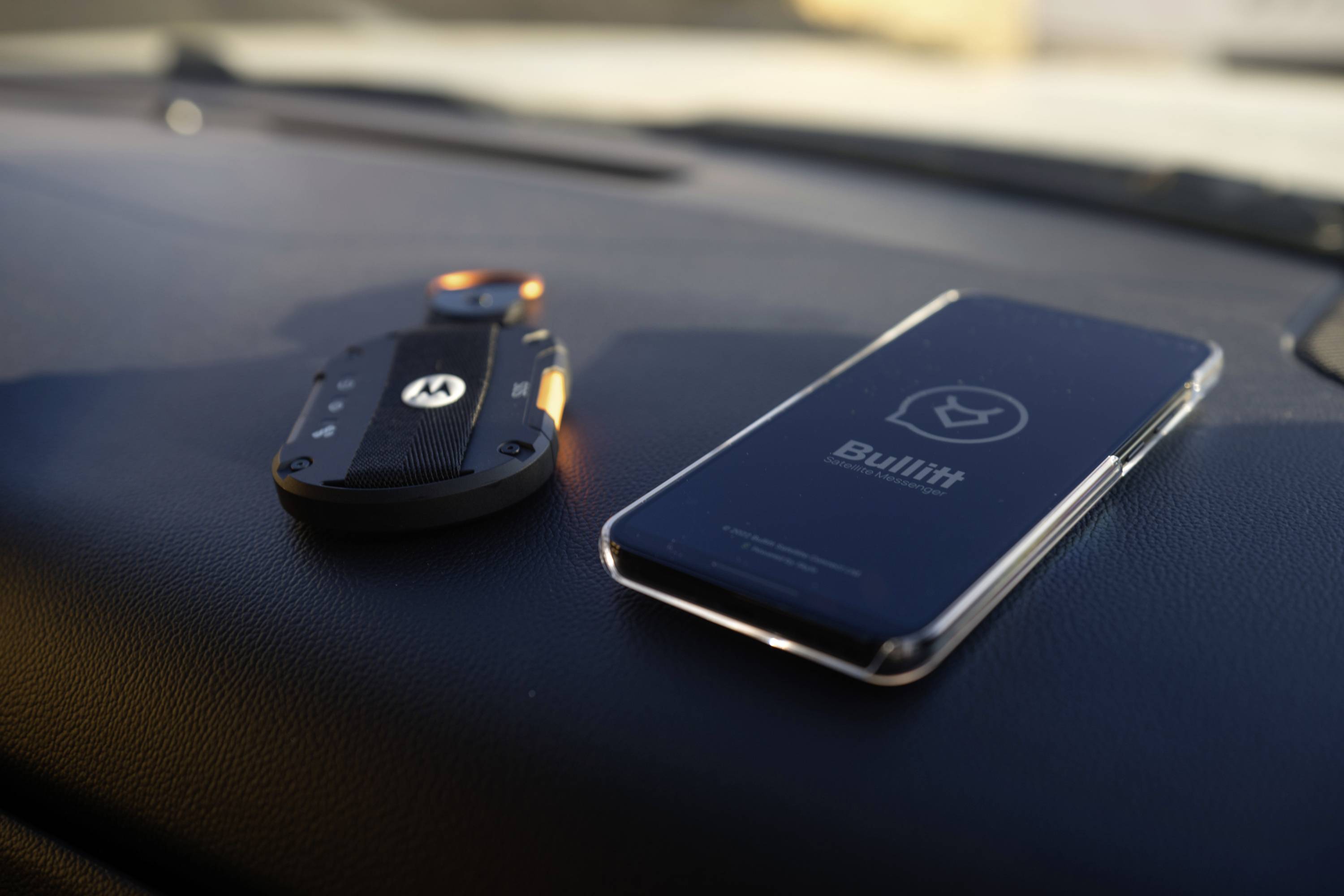 Een smartphone ligt naast een portofoon op een autodashboard. Op de mobiele telefoon staat 'Bullitt'.