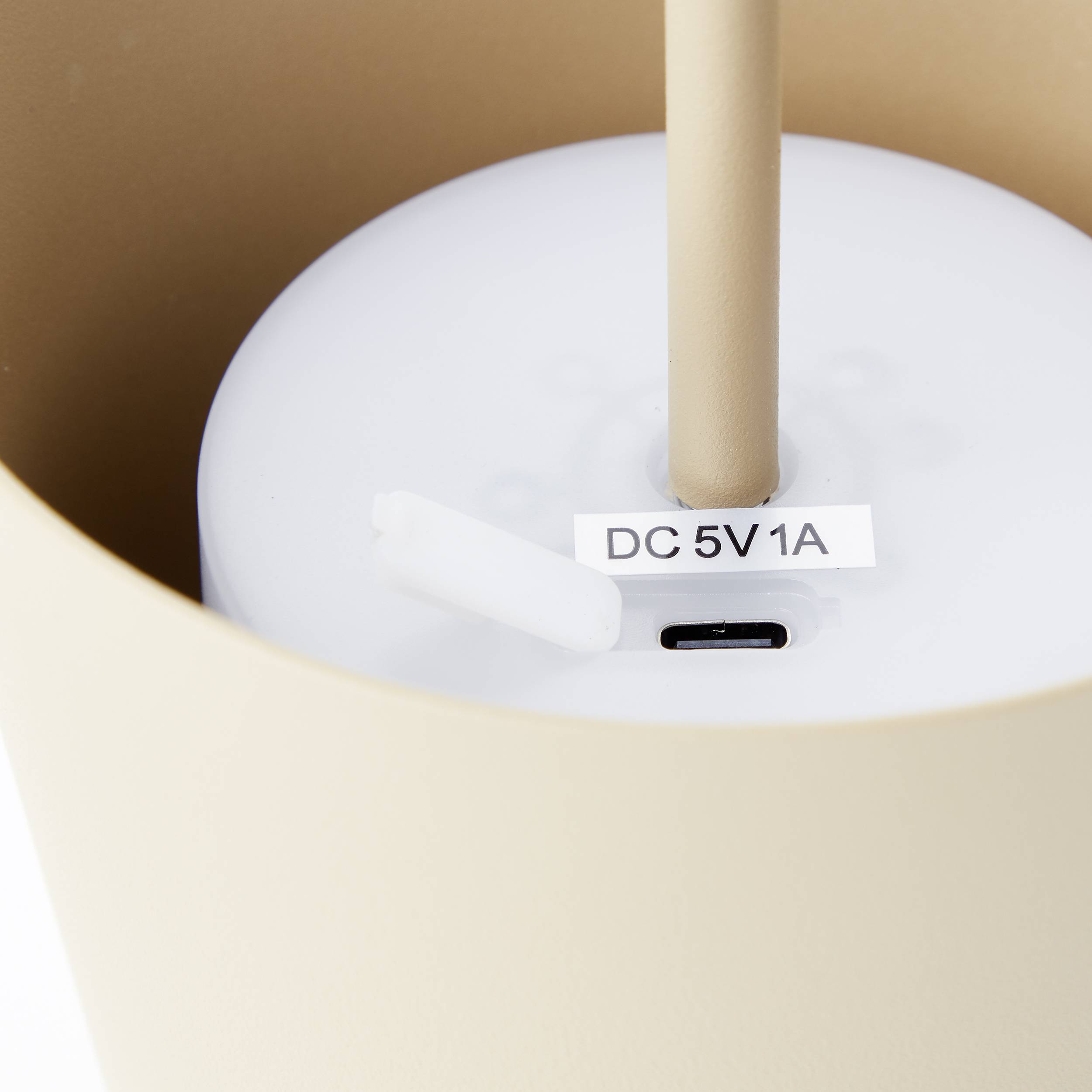 Een wit elektrisch apparaat met een 'DC 5V 1A'-aansluiting. Het staat in een crèmekleurige container.