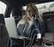 Een vrouw belt en werkt op een laptop in een auto. Meerdere apparaten zijn aangesloten op een oplader op de middenconsole.