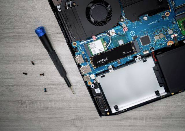Gedemonteerde binnenkant van een laptop met harde schijf en schroeven. Een schroevendraaier ligt ernaast.