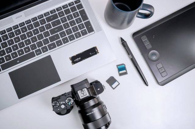 Laptop, digitale camera, grafisch tablet en mok op een tafel vanuit bovenaanzicht. Accessoires zoals geheugenkaart en pen zijn ernaast geplaatst.
