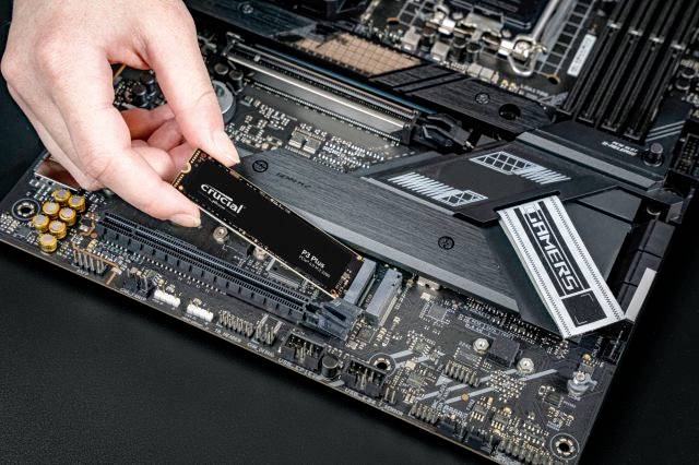 Een hand installeert een SSD op een moederbord. De SSD wordt in een M.2-sleuf geplaatst. De focus ligt op de montage.