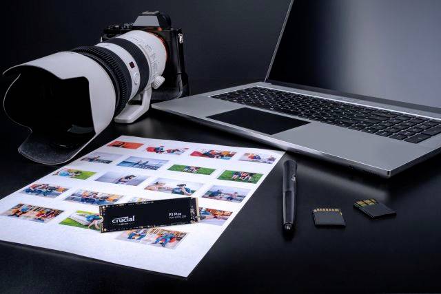 Een laptop, een camera met een groot objectief, foto's, een USB-stick en geheugenkaarten liggen op een tafel; toont techniek voor fotografie.