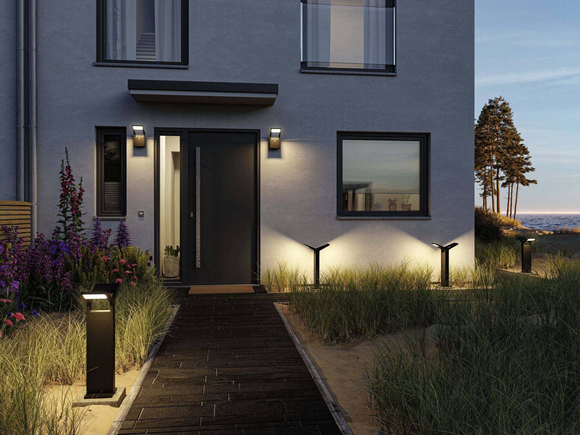 Een modern huis bij schemering, verlicht pad naar de ingang met planten en uitzicht op zee op de achtergrond.