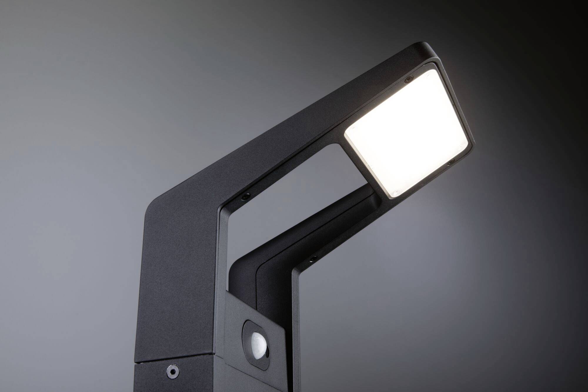 Een moderne zwarte LED-lamp met een vierkante lichtunit die naar beneden schijnt, gefotografeerd tegen een donkere achtergrond.