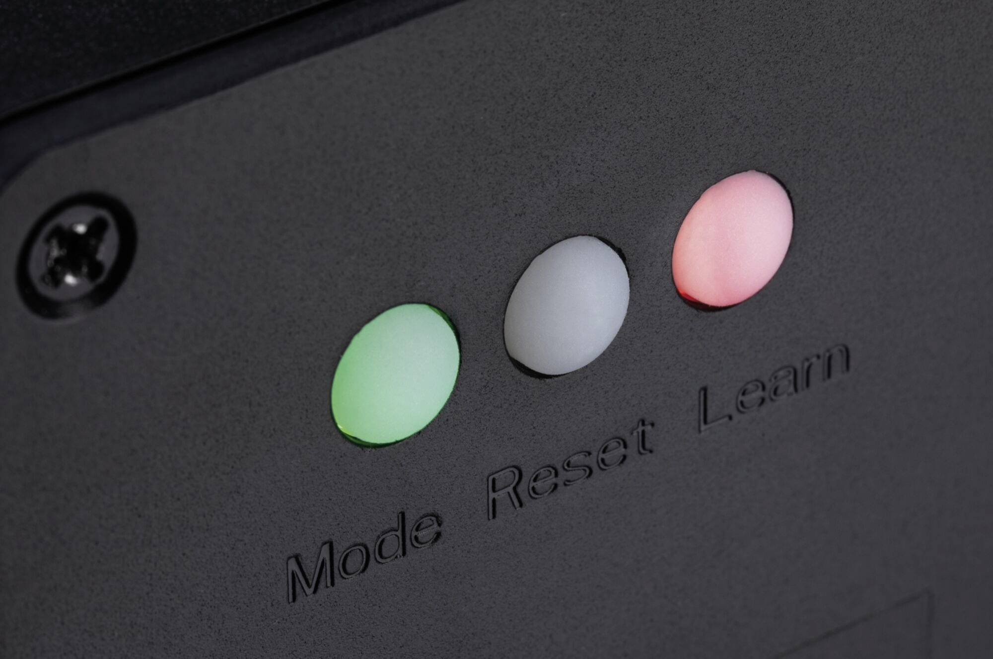 Zwartgrijs apparaat met drie knoppen: groen voor 'Modus', wit voor 'Reset', rood voor 'Leren'.
