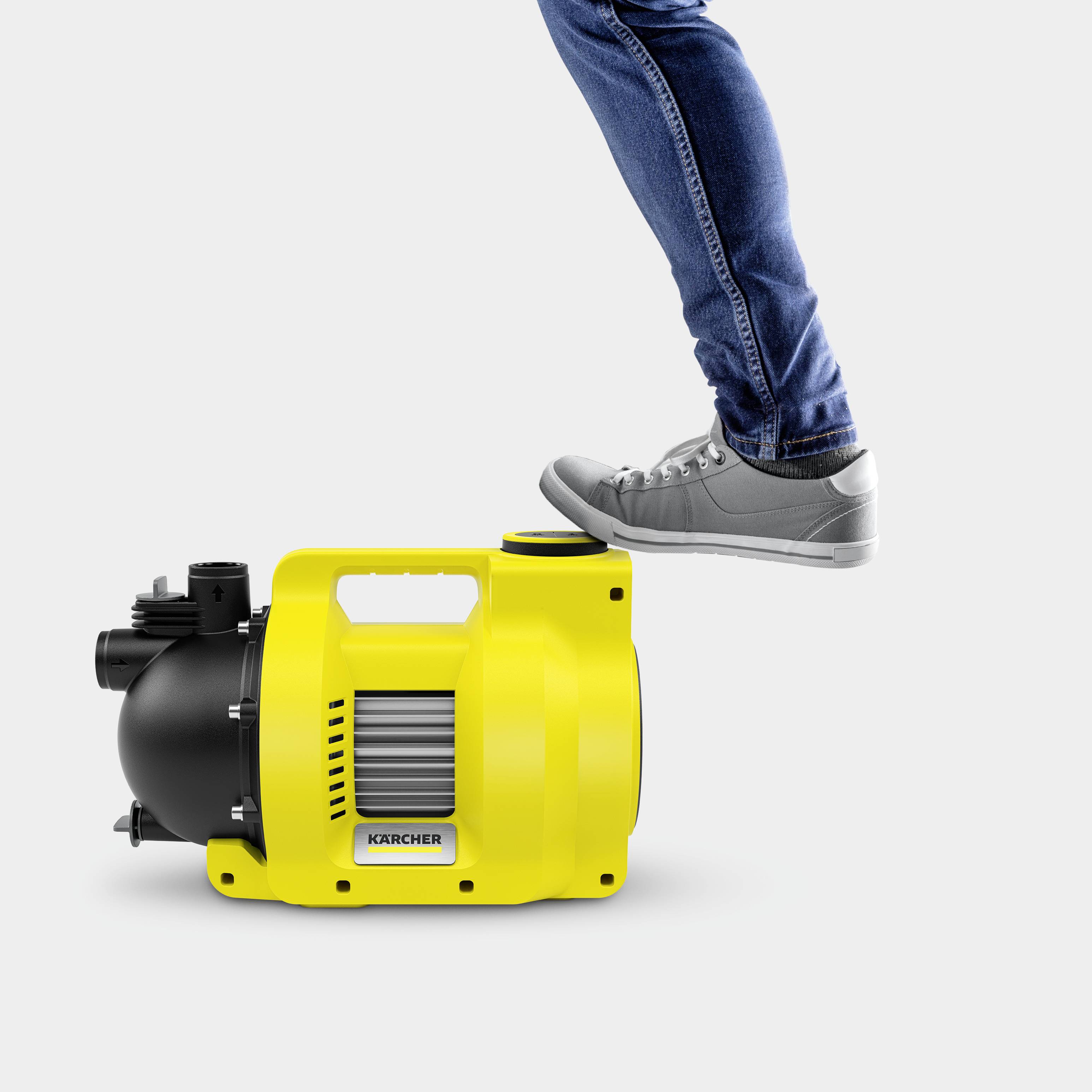 Een gele waterpomp van Kärcher wordt getest door een persoon die met zijn voet op de pomp staat om de stabiliteit ervan aan te tonen.