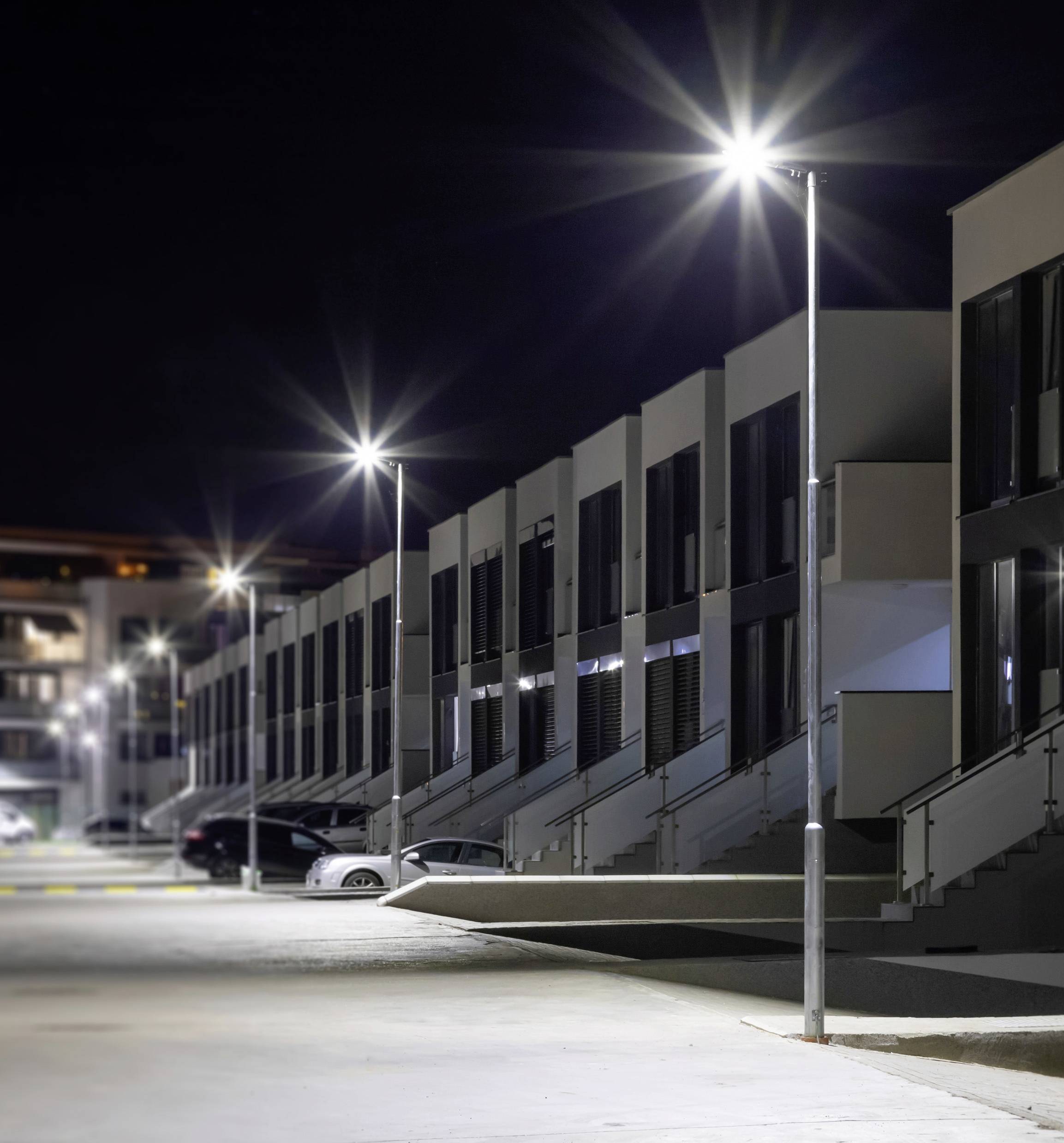 Rij moderne rijwoningen bij nacht, verlicht door heldere straatverlichting. Enkele auto's geparkeerd langs de straat.