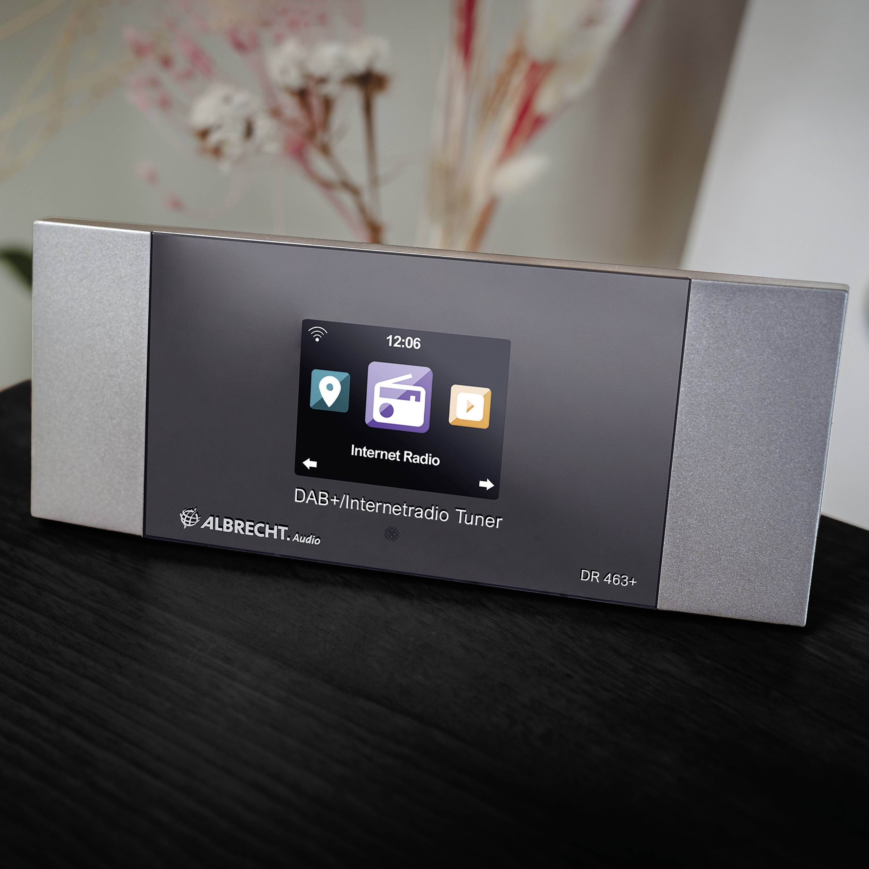 Een moderne DAB+/Internetradio-tuner met een digitale display staat op een tafel. Op het scherm zijn de tijd en symbool-iconen zichtbaar.
