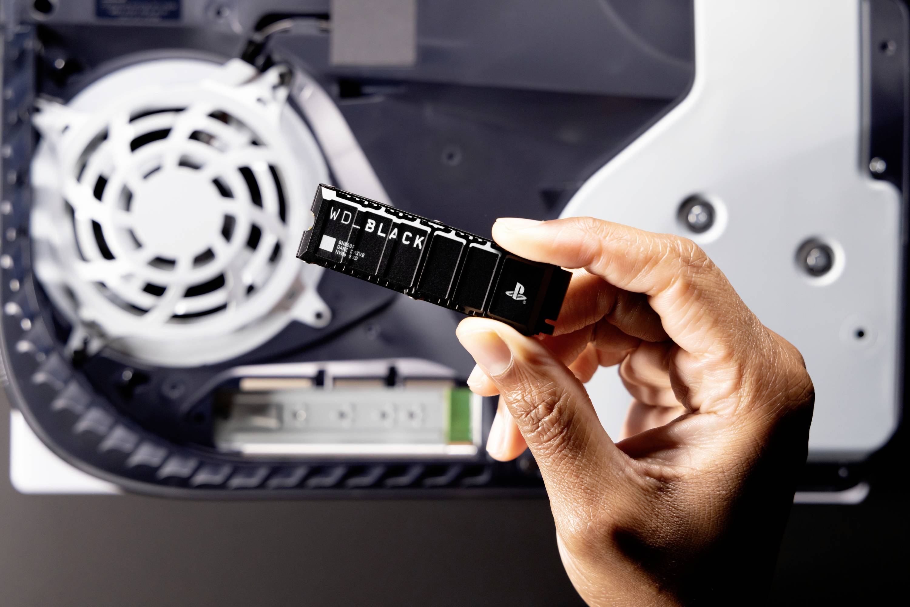 Een hand houdt een SSD-schijf vast voor een geopende computerbehuizing met een zichtbare ventilator.