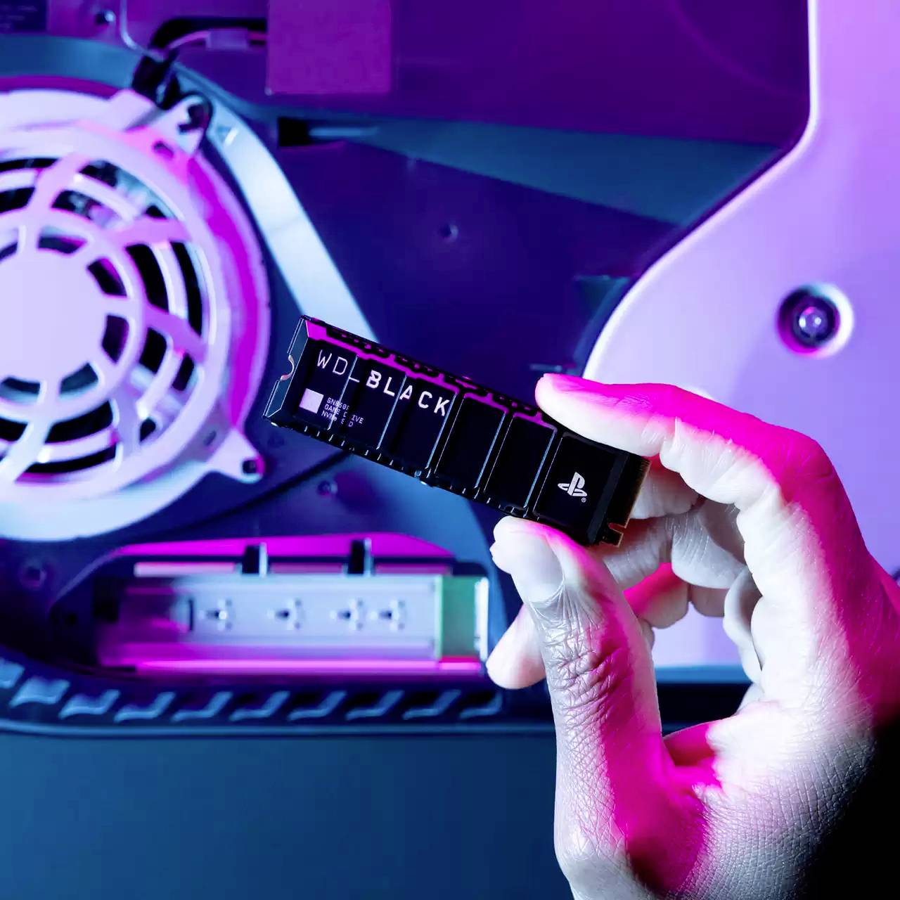 Een hand houdt een kleine zwarte opslagchip voor de achterwand van een geopend elektronisch apparaat met zichtbare ventilator.