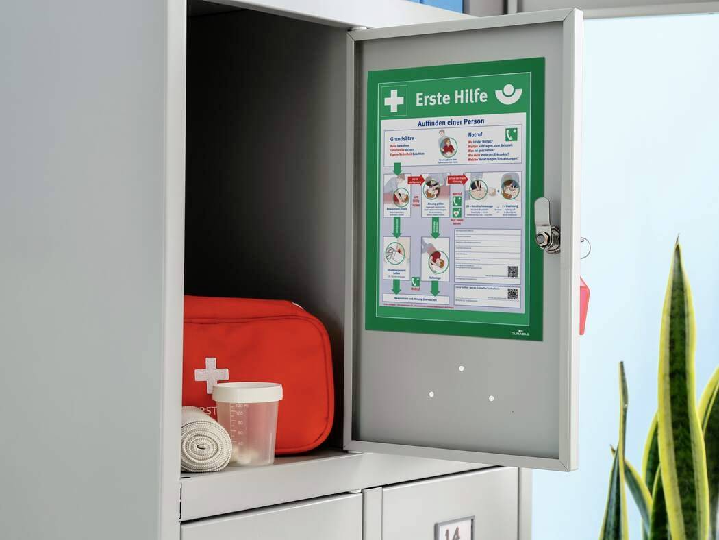 Een geopende EHBO-kast toont een EHBO-set met verband en beker. Aan de deur hangt een poster met instructies.