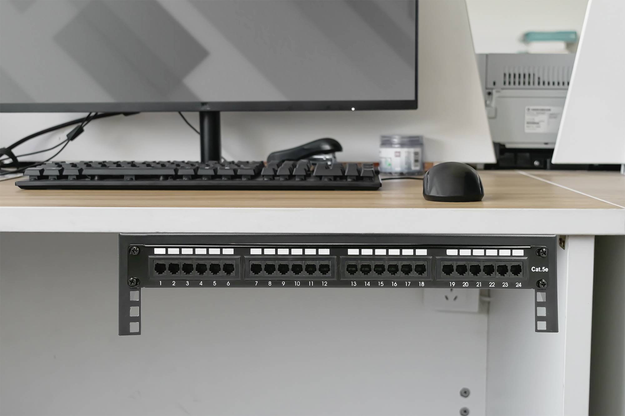 'Netwerk-switch gemonteerd onder een bureau, aangesloten op een computer. Muis en toetsenbord op het bureau.'