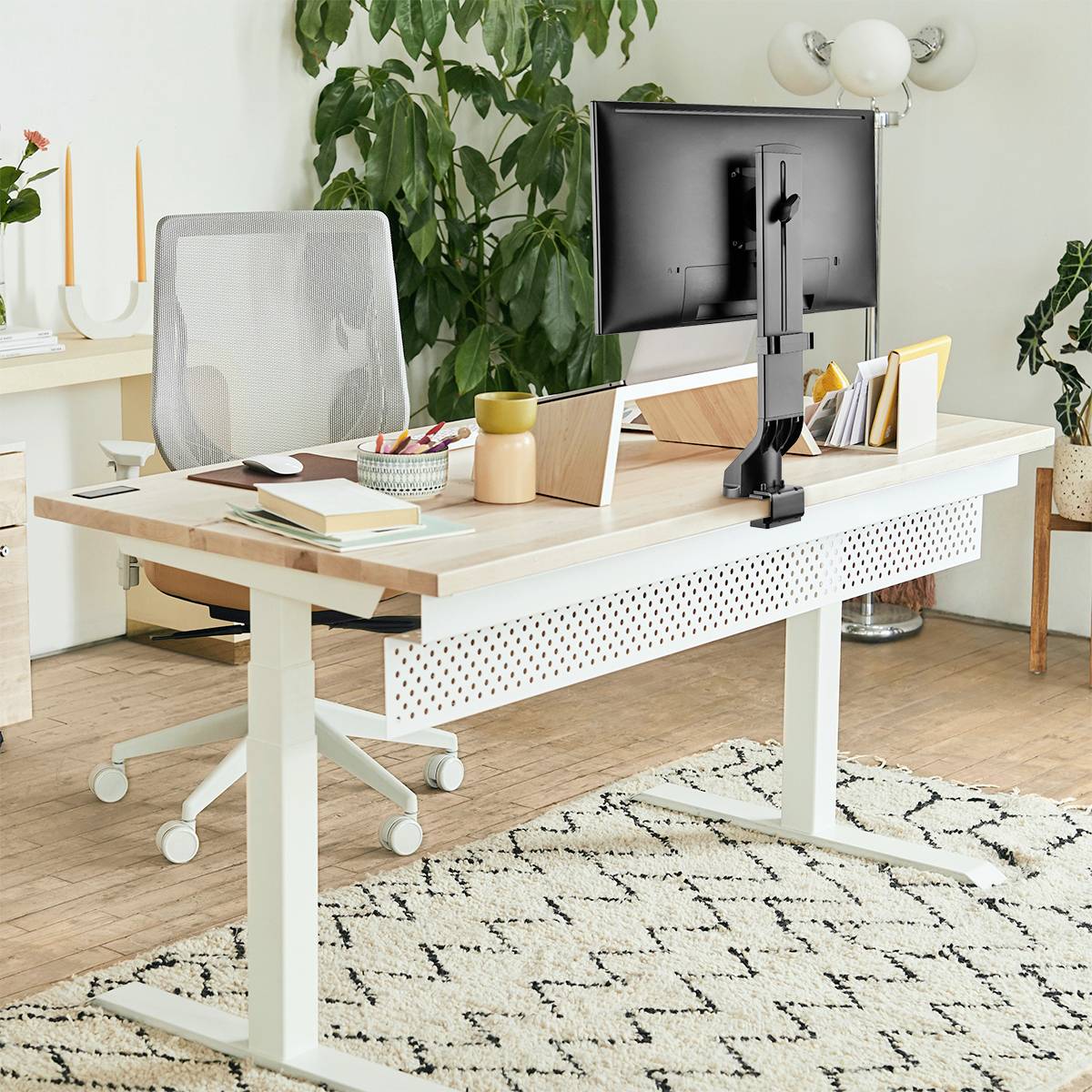 Een moderne werkplek met een bureau, computerscherm, bureaustoel en planten op de achtergrond. Lichte, minimalistische inrichting.