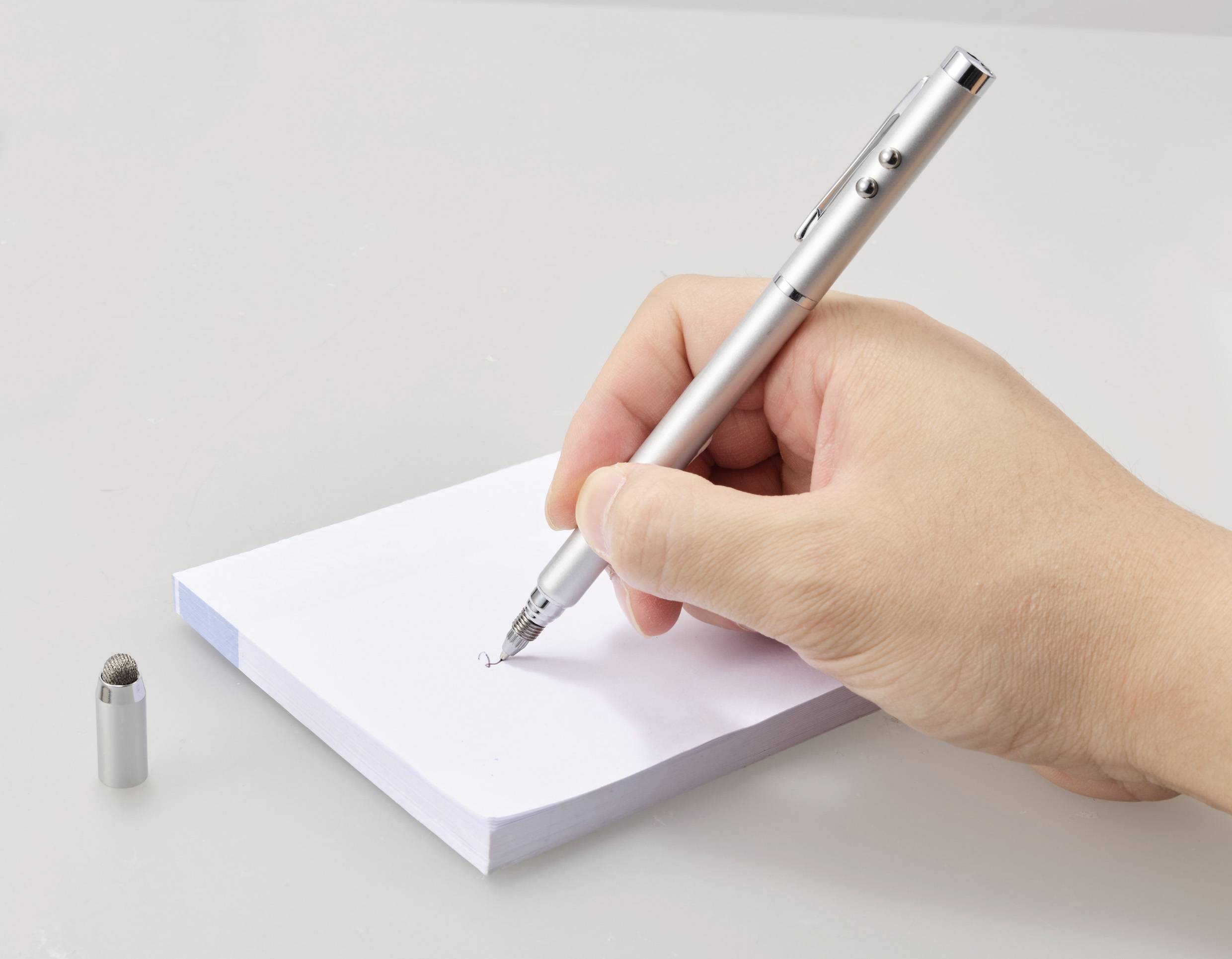 Een hand schrijft met een zilveren pen op een notitieblok. De dop van de pen ligt ernaast.