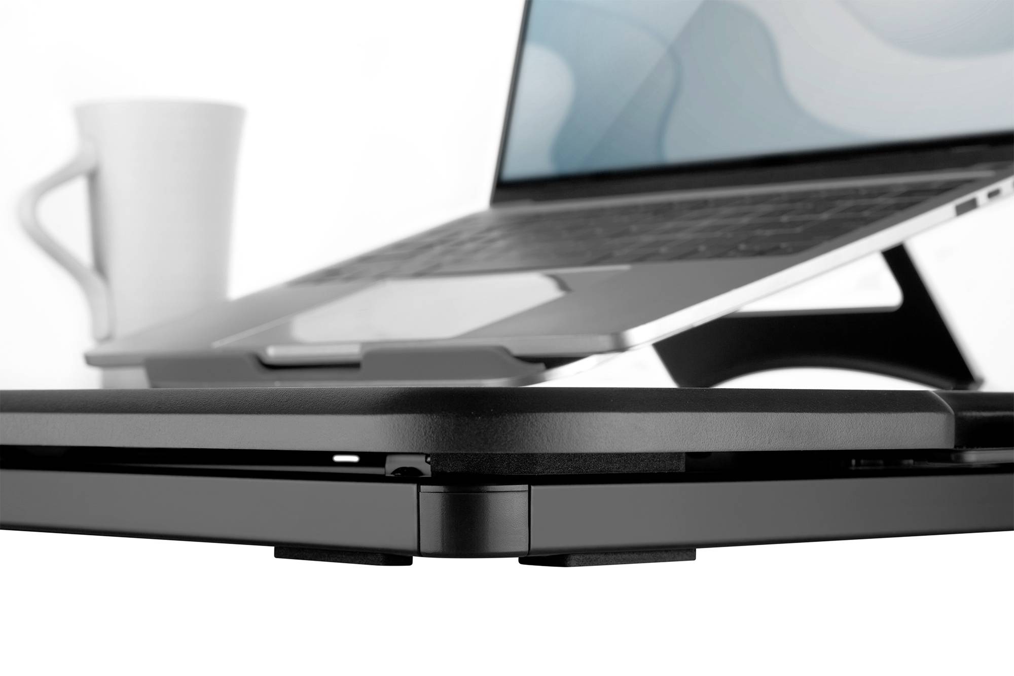 Een laptop op een standaard, naast een witte mok. Het scherm toont een onherkenbaar patroon.