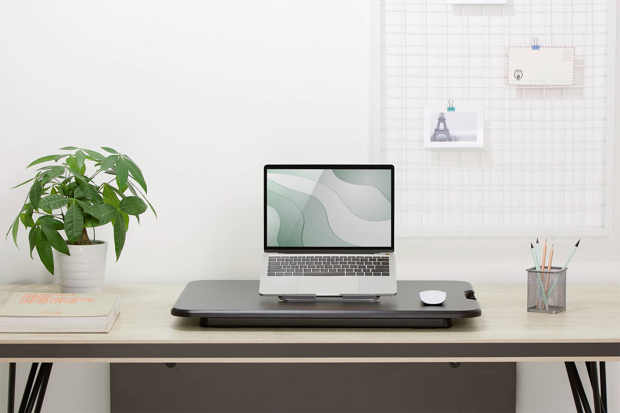 'Een opgeruimd bureau met een laptop, een muis, een plantenpot en schrijfwaren, voor een witte rasterachtergrond met kaarten.'