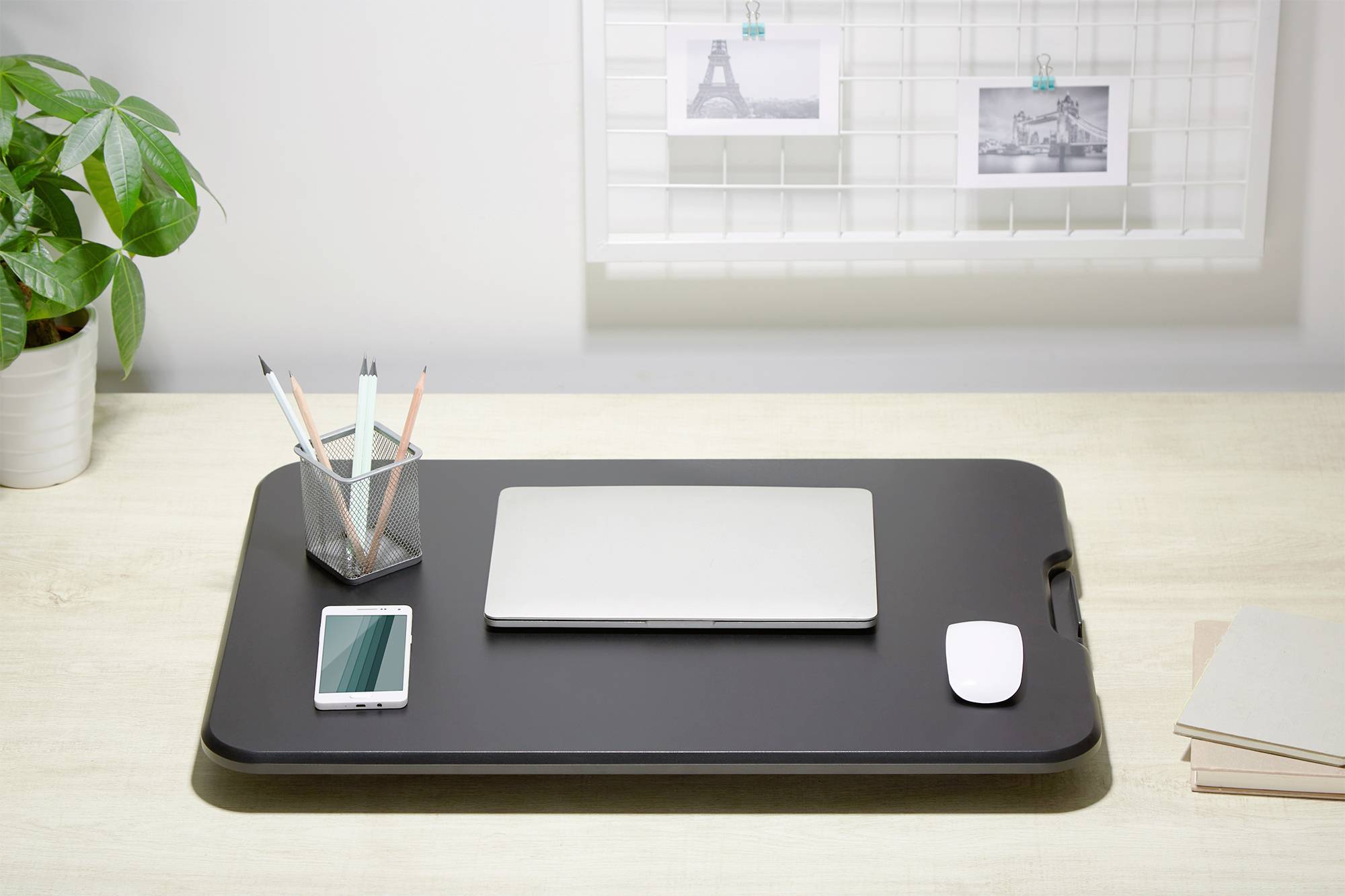 Een nette bureau met laptop, muis, smartphone en een pennenhouder. Op de achtergrond zijn twee ingelijste foto's te zien.