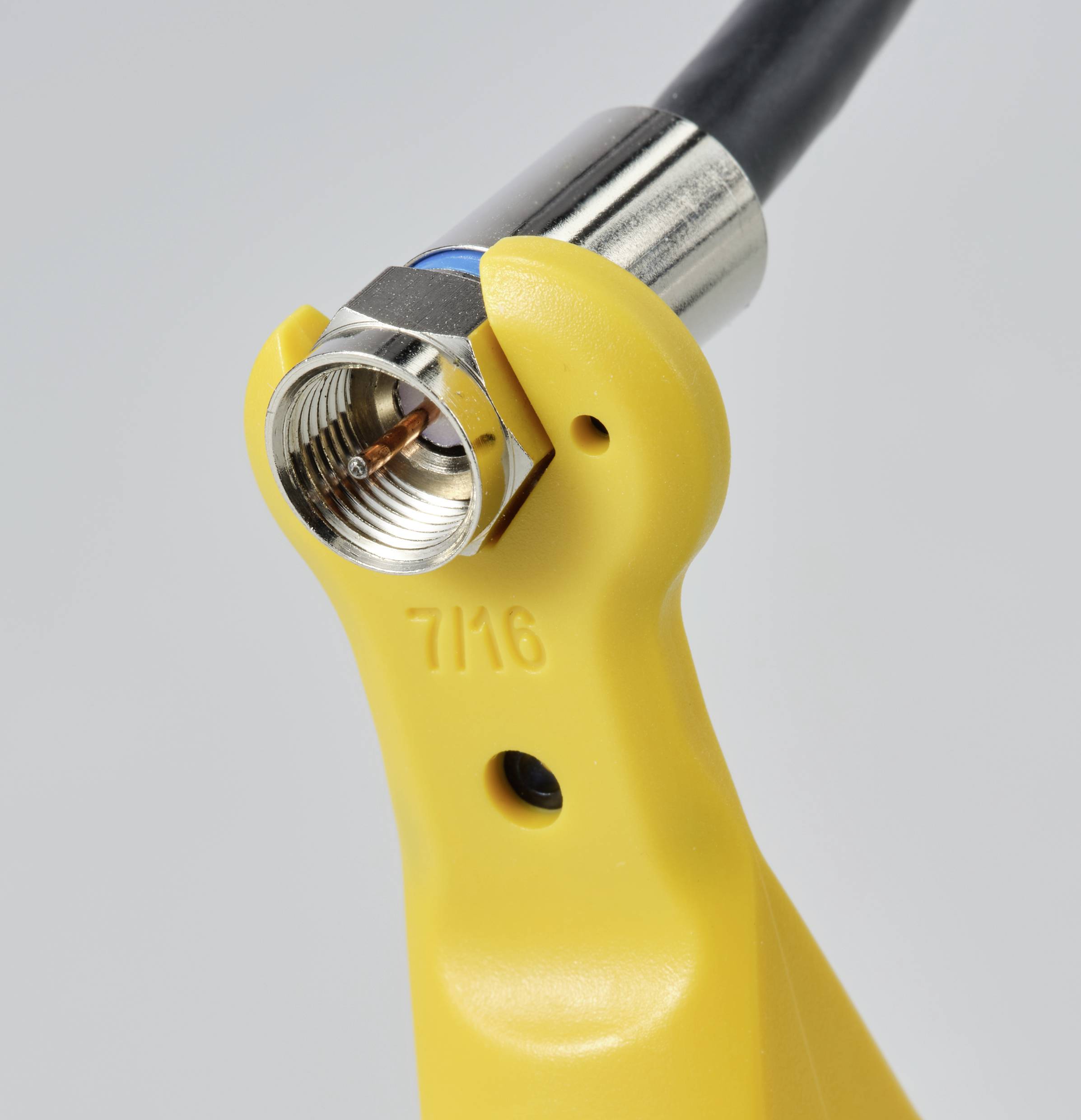 Een gele sleutelhouder bevestigt een coaxiale stekker aan een kabel, klaar voor installatie.