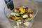 Een glazen kom met vers gesneden groenten zoals courgette, paprika en champignons op een houten tafel.