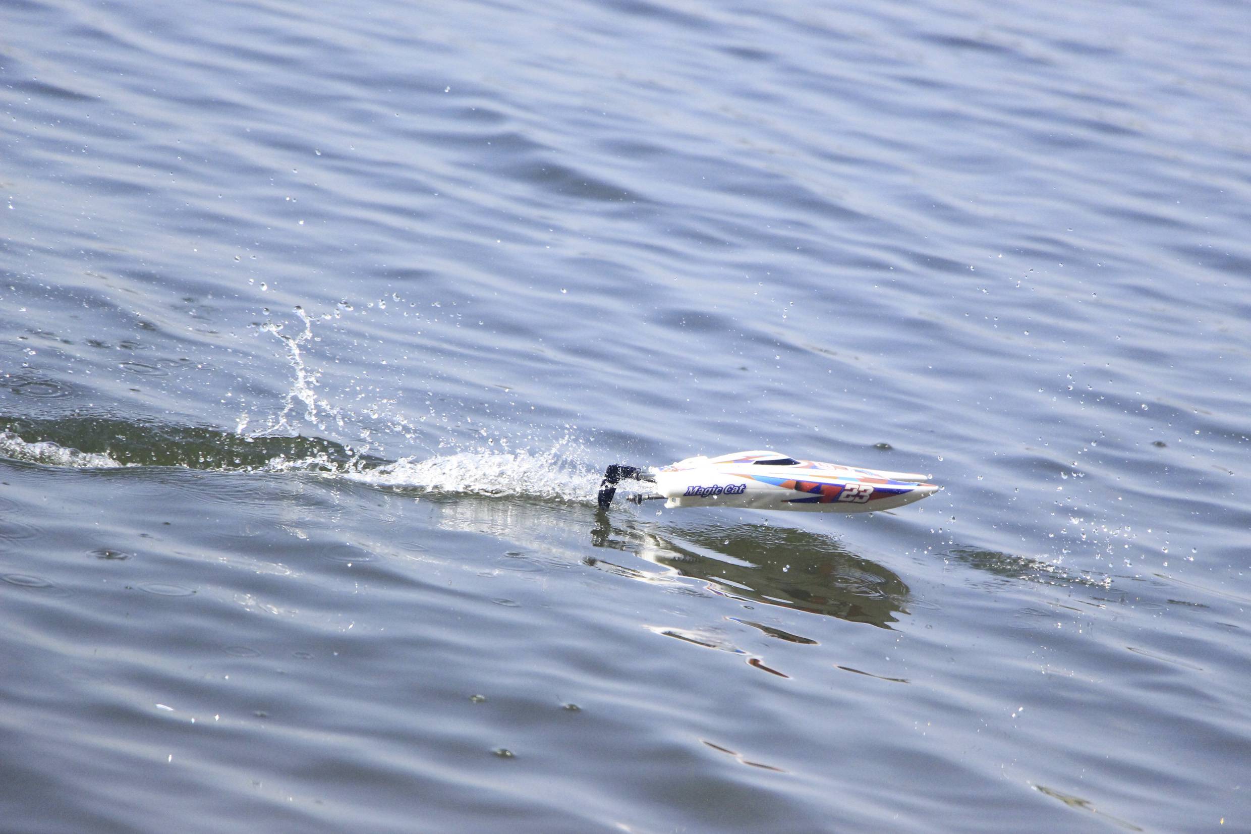 Een klein modelbootje glijdt snel over het wateroppervlak, trekt golven achter zich aan en spat water op.