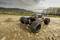 Een op afstand bestuurbare auto met grote banden rijdt over een rotsachtig pad in een landelijk landschap. Op de achtergrond zijn velden en bomen zichtbaar.