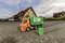 Speelgoed-vuilniswagen en vuilnisbak op een straat voor woningen. De vrachtwagen is oranje-groen met een milieuboodschap.