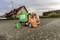 Speelgoed-vuilniswagen op een straat voor huizen. De oranje vrachtwagen heeft een groene container met milieugerelateerde motieven.