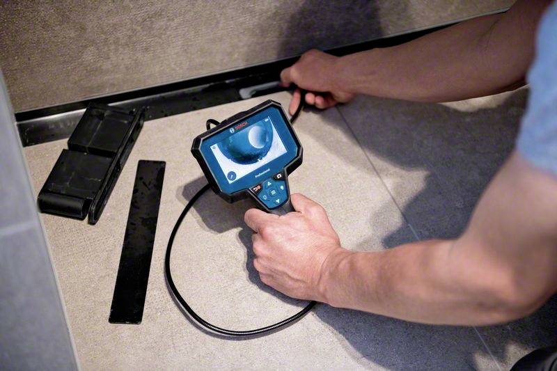 Een persoon gebruikt een inspectiecamera-apparaat om onder een oppervlak te kijken. Aangrenzende gereedschappen en kabels zijn zichtbaar.