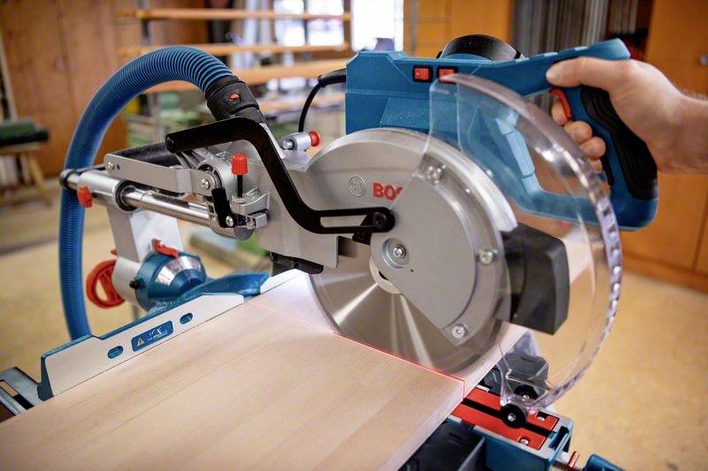 Een cirkelzaag zaagt een houten plank. Een persoon houdt de zaag met één hand vast. De zaag heeft een beschermkap.