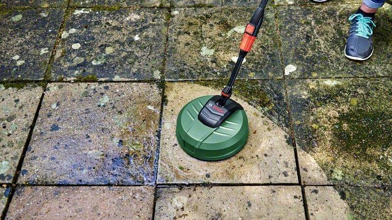 Een persoon reinigt een sterk vervuilde terras met een hogedrukreiniger. Links is het oppervlak schoon, rechts nog vies.