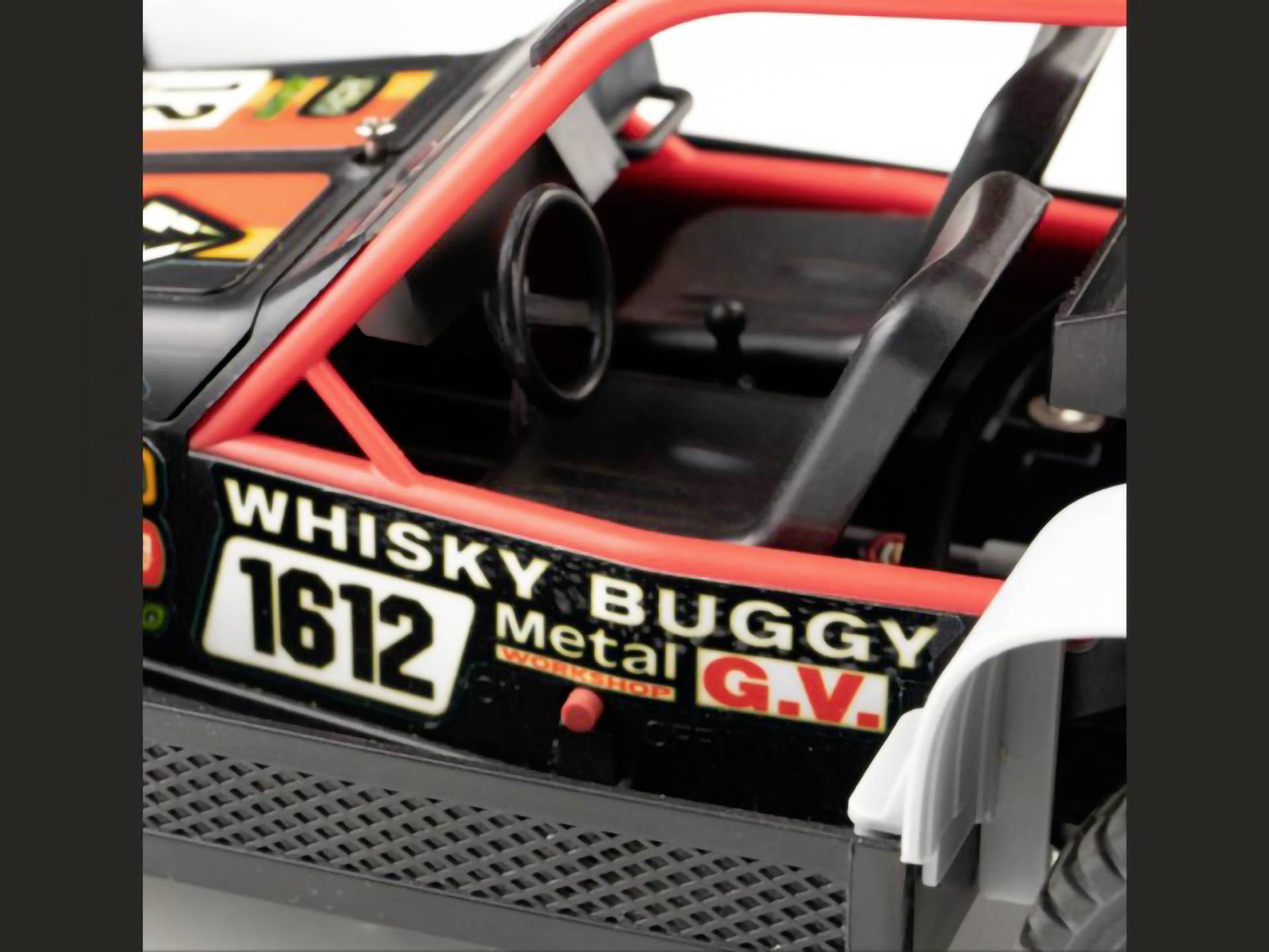 Close-up van een speelgoed-buggy met de tekst 'Whisky Buggy Metal G.V. 1612' aan de zijkant. Stuur en zitting zijn zichtbaar.