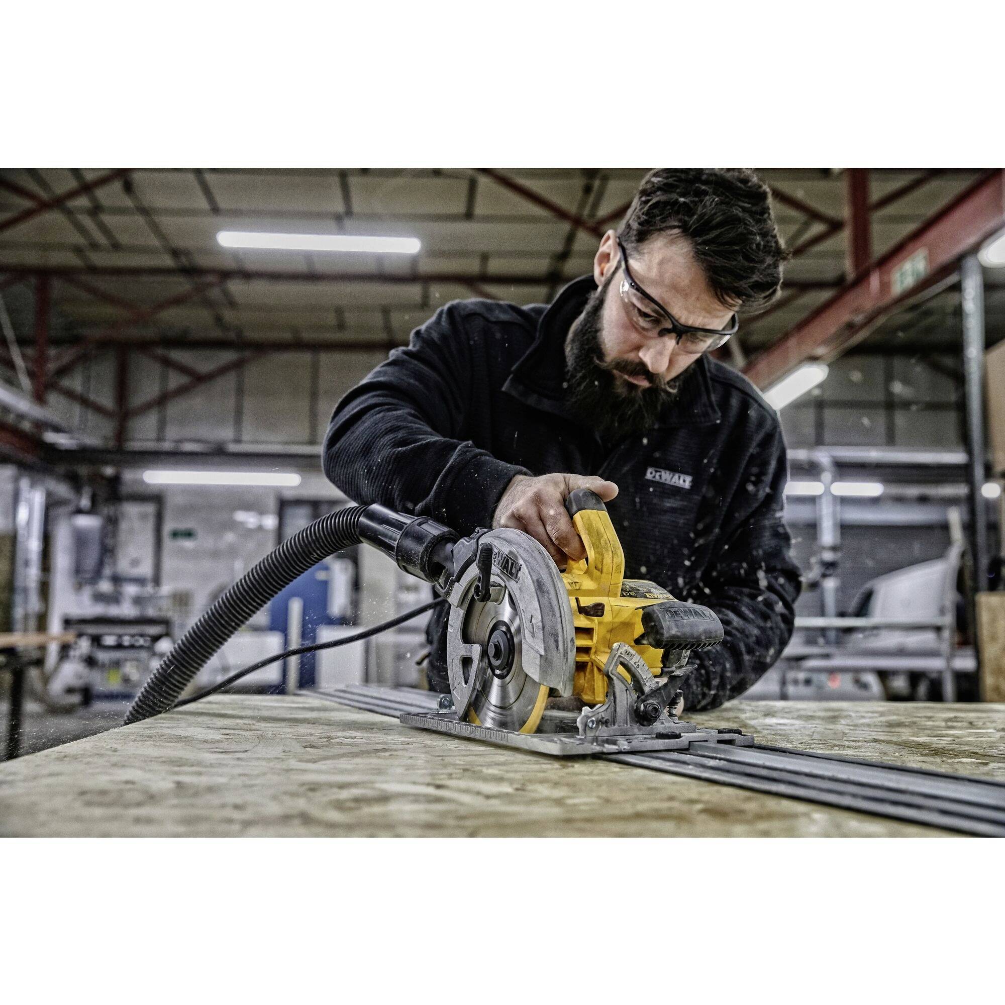 Een persoon draagt een veiligheidsbril en gebruikt een cirkelzaag om een plank te zagen in een werkplaatsomgeving.