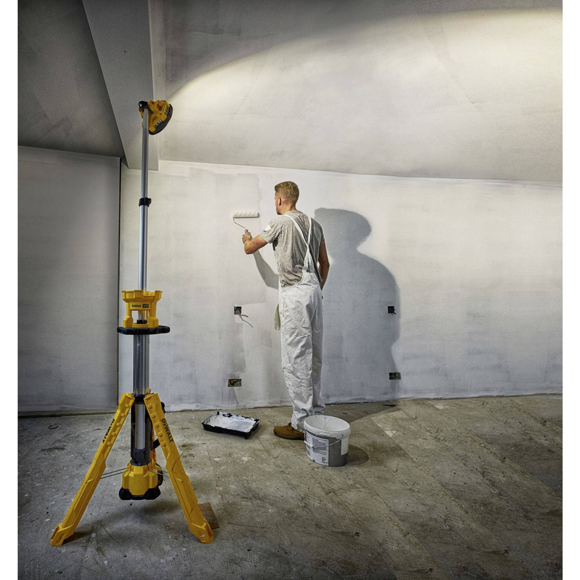 'Een schilder in witte werkkleding schildert een muur met een verfroller. Een bouwlamp verlicht de ruimte.'