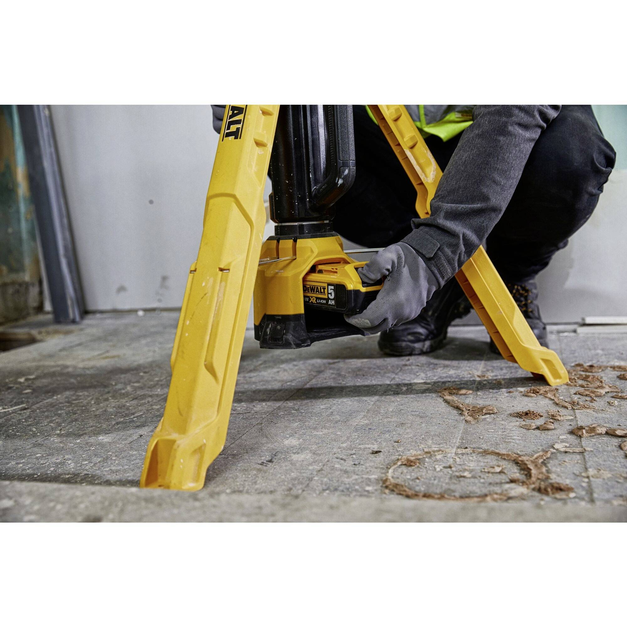 'Arbeider met handschoenen plaatst geel bouwapparaat op betonvloer, details van voeten en gereedschap zichtbaar.'