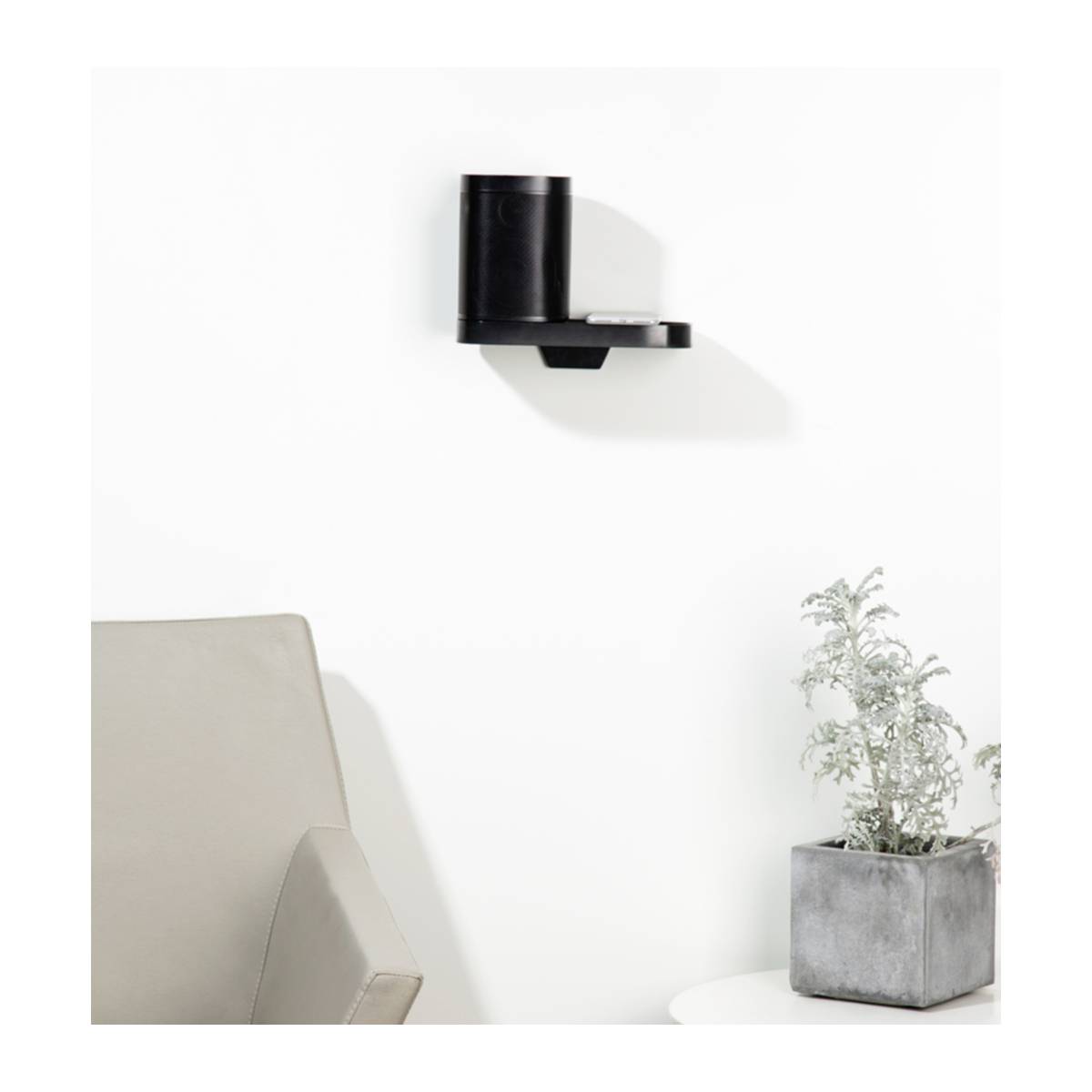 Zwart wandrek met een ronde vaas erop. Ernaast een hoekbank en een kleine, witte tafel met een potplant. Lichte muur op de achtergrond.