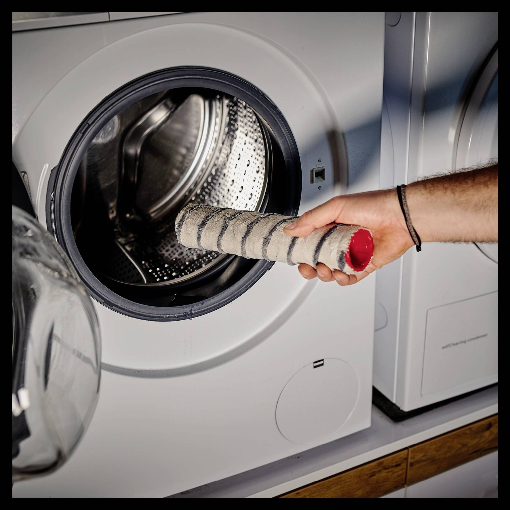 Iemand reinigt de wasmachine door het pluizenzeefje in zijn hand vast te houden om het te inspecteren.