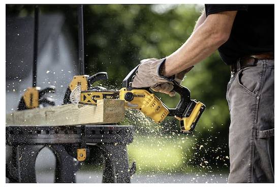 'Een persoon die een elektrische zaag gebruikt om een houten plank door te zagen op een werkbank buiten, waarbij zaagsel rondvliegt terwijl de zaagblad door het hout beweegt.'