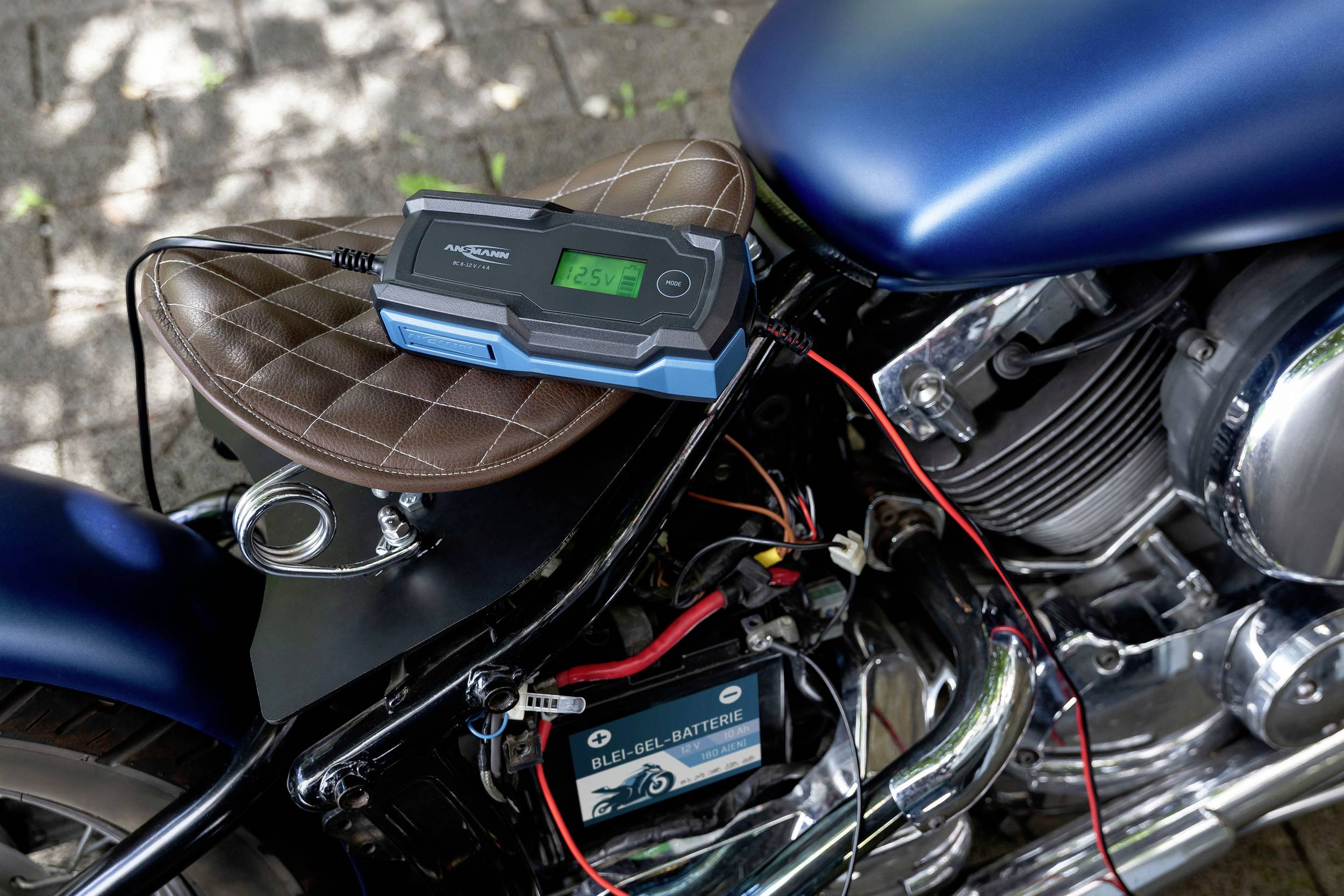 Een motorfiets met een aangesloten batterij en een oplader die op de zitting ligt. Het display toont de laadstatus.