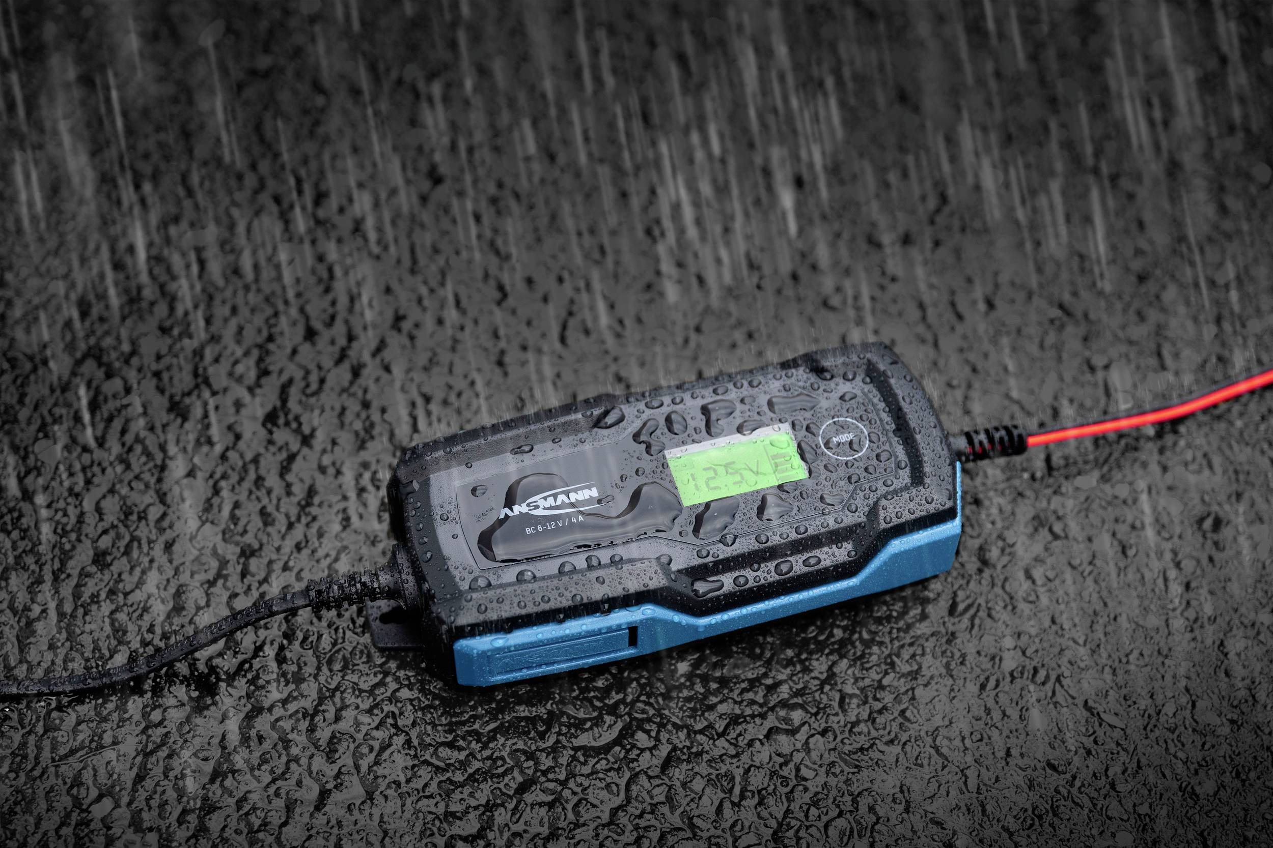 Een batterijlader op een natte ondergrond in de regen, met een verlicht display dat informatie weergeeft.