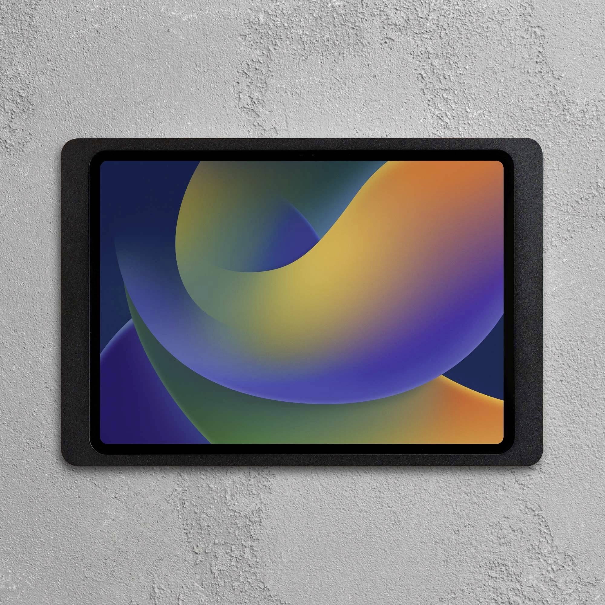 Een tablet met een kleurrijke, abstracte grafiek op het scherm. Het hangt aan een grijze betonnen muur.