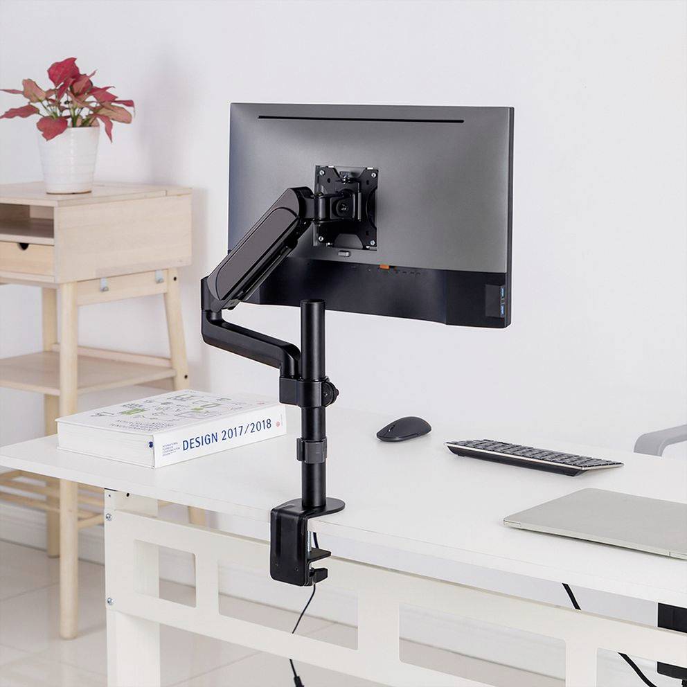 Een moderne bureaumonitor bevestigd aan een verstelbare arm, op een wit bureau. Op de achtergrond een plant op een houten kast.