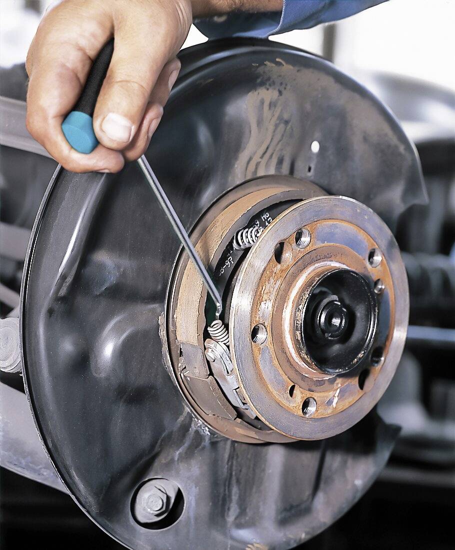 Een persoon repareert een rem aan een voertuig door met een schroevendraaier te werken aan de veer en de remblok.