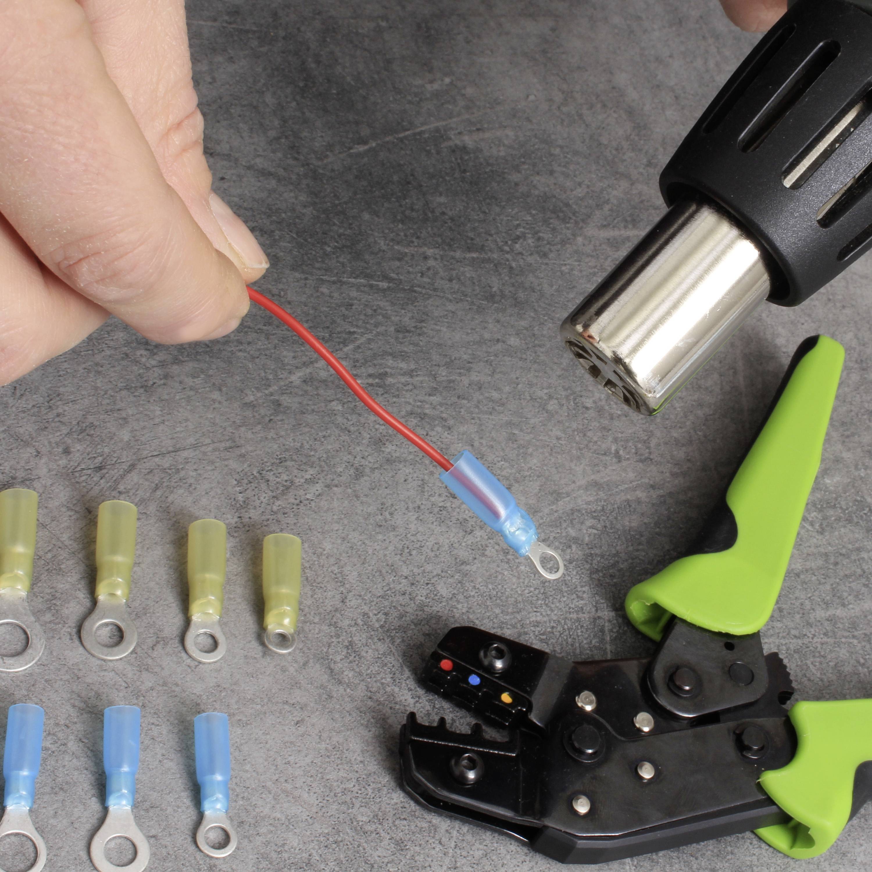 Een persoon gebruikt een krimpkous om een kabel te isoleren. Op tafel liggen krimpverbinders en een krimptang.