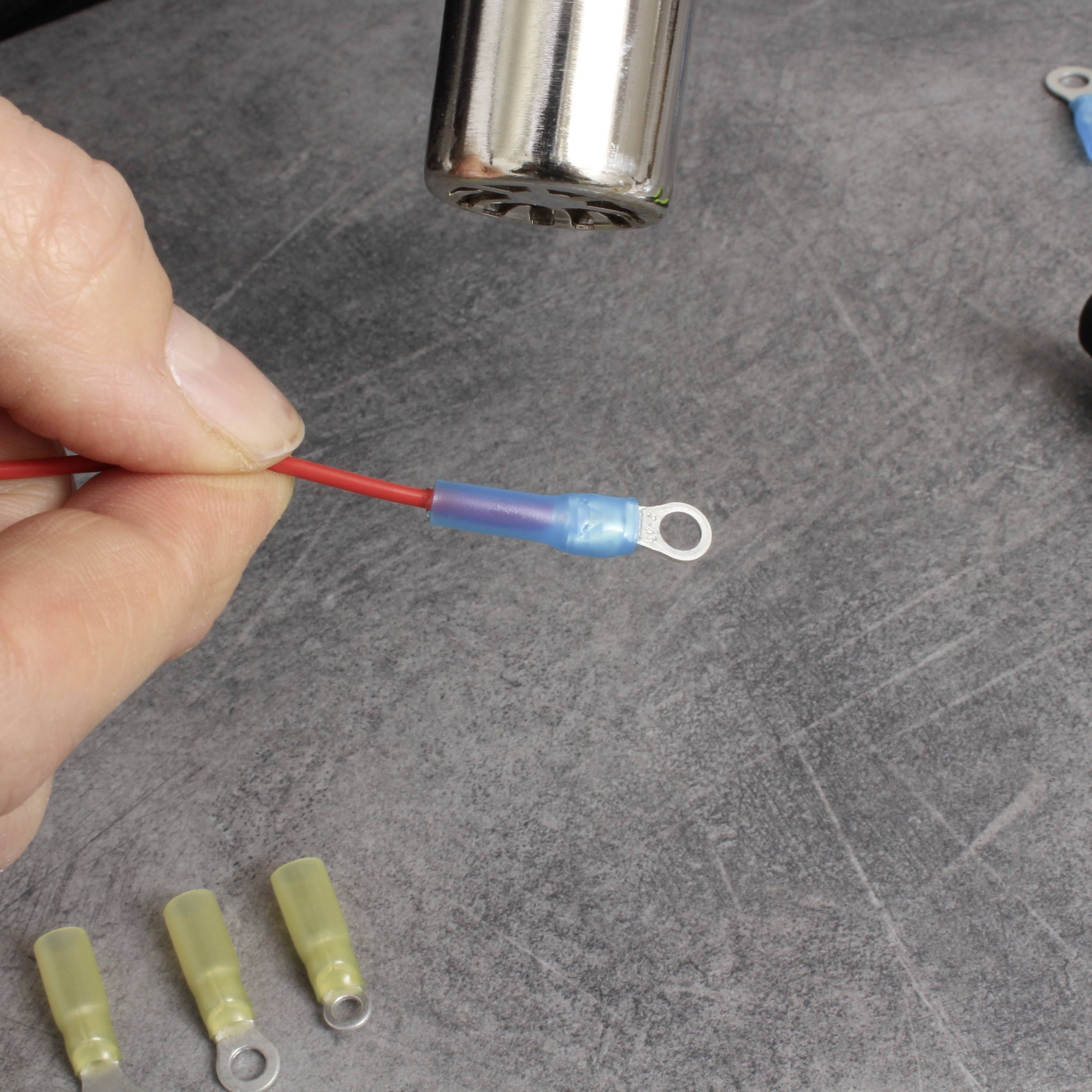 Een hand houdt een rood kabel vast met een blauwe, geïsoleerde kabelschoenaansluiting. Een zilveren gereedschap wordt boven het kabel gehouden.