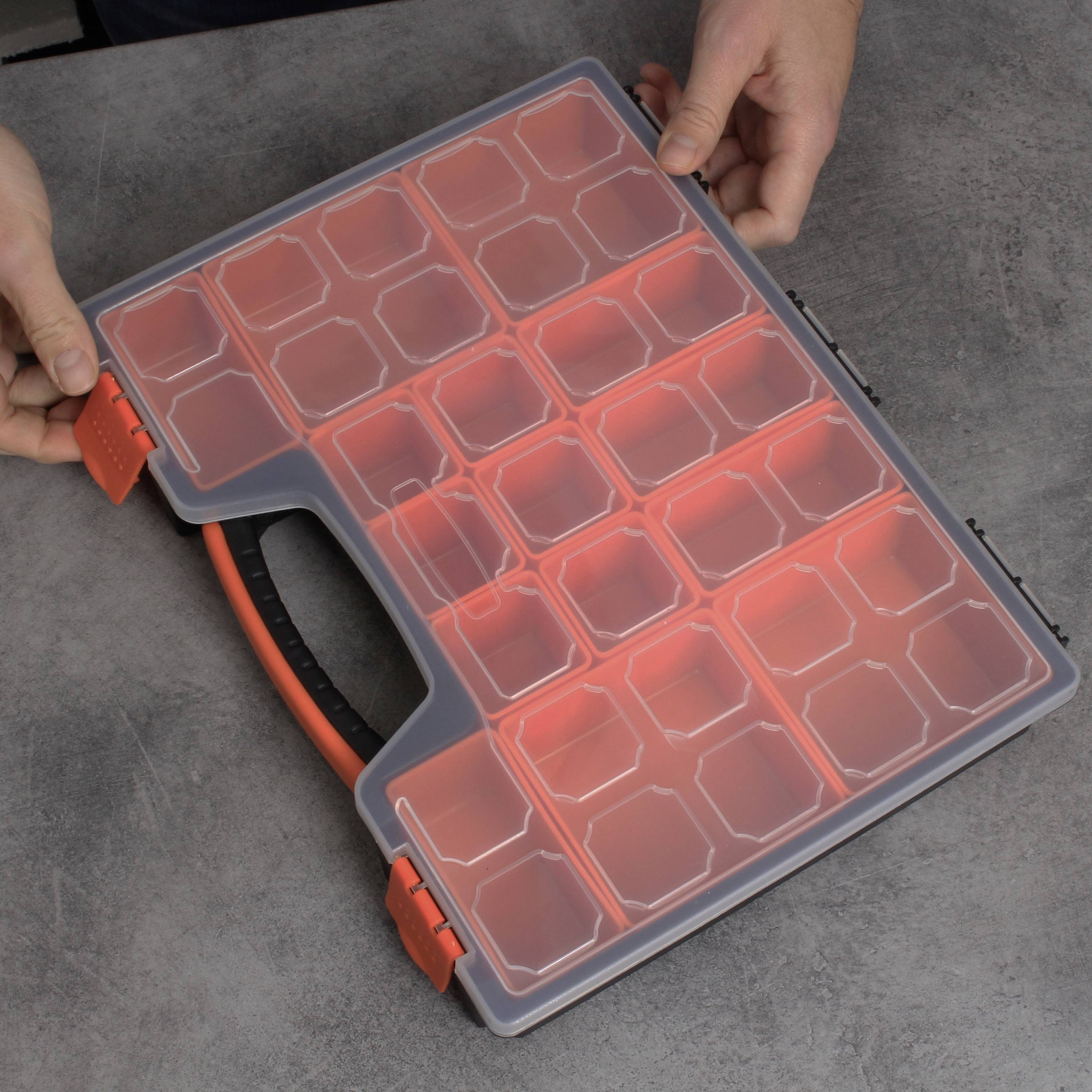 Een persoon opent een grijze en oranje organizer-box met meerdere vakken, die op een grijze tafel ligt.
