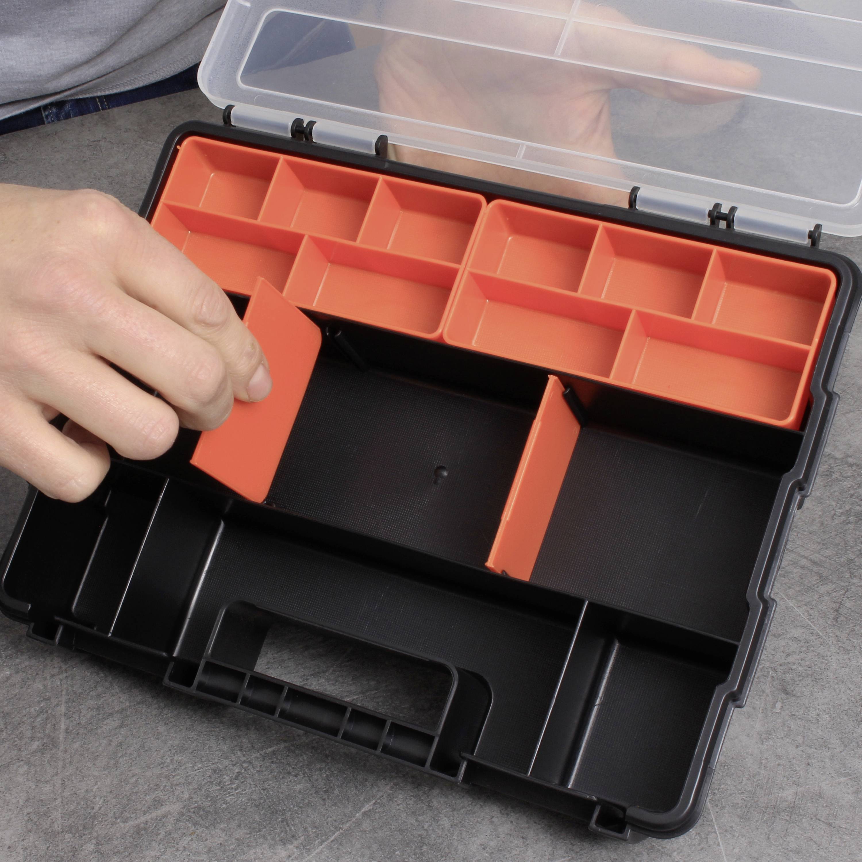 Een hand opent een lege zwarte gereedschapskist met rode, uitneembare vakken op een grijze tafel.